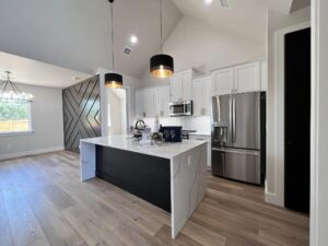 Modern kitchen with a black and white color scheme. Features include a central island with a white countertop, high-end stainless steel appliances, pendant lights, and wooden floor panels. Adjacent dining area with a geometric accent wall and chandelier.